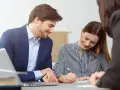 Un homme et une femme souriants discutent d'un contrat de travail étudiant. Un ordinateur portable est visible sur la table.