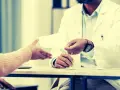 Un médecin remet un document, peut-être une suspension des indemnités journalières par le médecin conseil, à un patient.