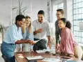Une équipe souriante discute autour d'une table, partageant des documents. L'ambiance est détendue, comme lors d'un entretien de fin de mandat réussi.