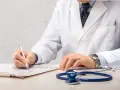Médecin en blouse blanche rédigeant un rapport, stéthoscope à proximité. Un signalement médecine du travail est en cours.
