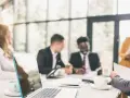 Une équipe discute lors d'une réunion CSE. Un ordinateur portable est ouvert sur la table, avec des tasses de café et des documents.