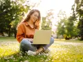 Jeune femme souriante travaillant sur son ordinateur portable dans un parc fleuri, explorant ses options pour l'âge légal pour travailler.
