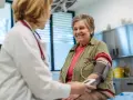 Une femme âgée souriante passe un examen de prévention santé. Le médecin lui prend la tension artérielle.