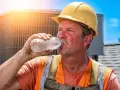 Ouvrier en sueur, casque jaune, buvant de l'eau sous un soleil de plomb. La condition de travail difficile est évidente sur son visage rougi.