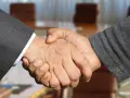 Poignée de main entre deux hommes en costume, scellant un accord. Leurs mains se serrent fermement, symbolisant la confiance et le partenariat.