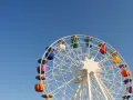 Grande roue colorée sous un ciel bleu clair, avec la lune visible. Une vue qui donne envie de monter, pour un asc cse inoubliable.