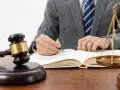 Un avocat en costume écrit dans un livre de droit, marteau de juge et balance de la justice à proximité. Une scène symbolisant l'entrave au CSE.