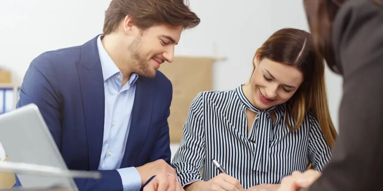 Un homme et une femme souriants discutent d'un contrat de travail étudiant. Un ordinateur portable est visible sur la table.