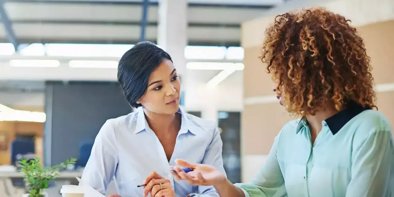 Deux femmes discutent au bureau. L'une semble expliquer les 5 obligations de l'employeur à l'autre.
