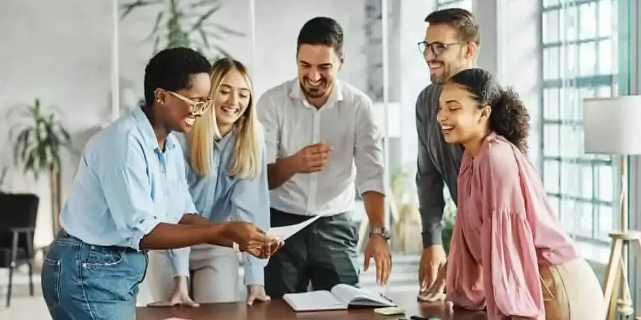 Une équipe souriante discute autour d'une table, partageant des documents. L'ambiance est détendue, comme lors d'un entretien de fin de mandat réussi.