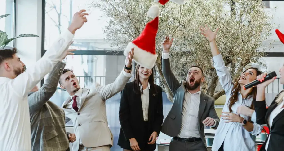 Des employés lancent des bonnets de Père Noël en l'air, célébrant joyeusement leur repas de Noël d'entreprise.