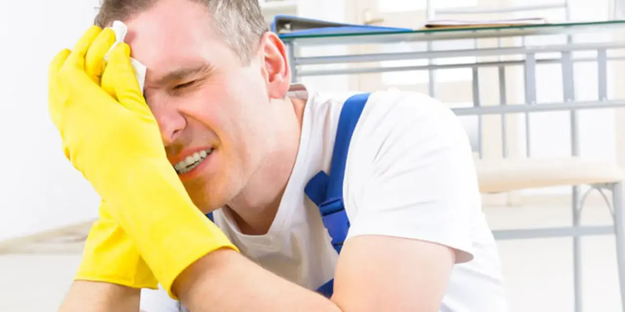 Homme en bleu de travail, gants jaunes, essuyant son front avec un mouchoir. Il semble souffrir, peut-être suite à un refus d'indemnité temporaire d'inaptitude.