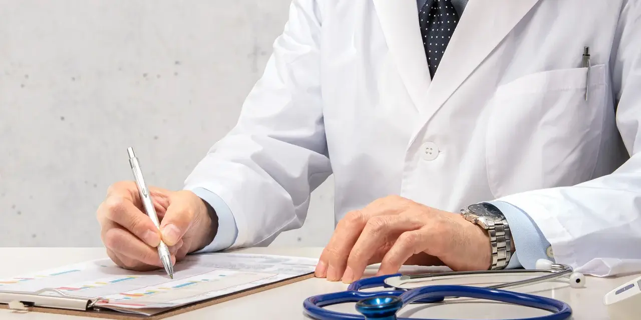 Médecin en blouse blanche rédigeant un rapport, stéthoscope à proximité. Un signalement médecine du travail est en cours.