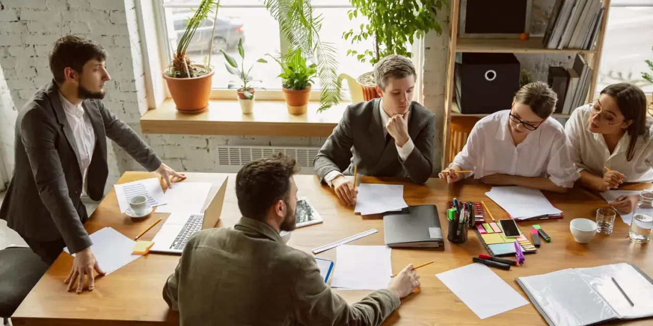 Une équipe discute autour d'une table dans un bureau lumineux, illustrant le concept de **flex office** : collaboration et adaptabilité.