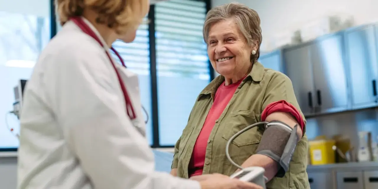 Une femme âgée souriante passe un examen de prévention santé. Le médecin lui prend la tension artérielle.