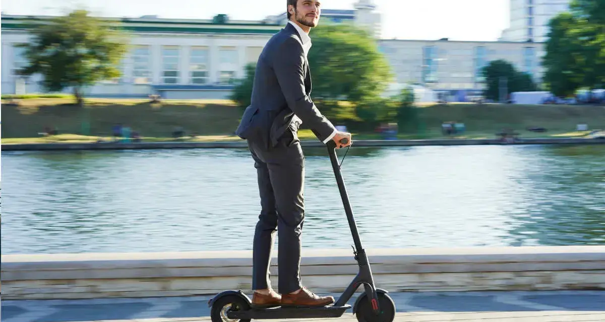 Homme en costume sur trottinette électrique, profitant de la liberté de mouvement. Une nouvelle façon de gérer la loi distance travail domicile.