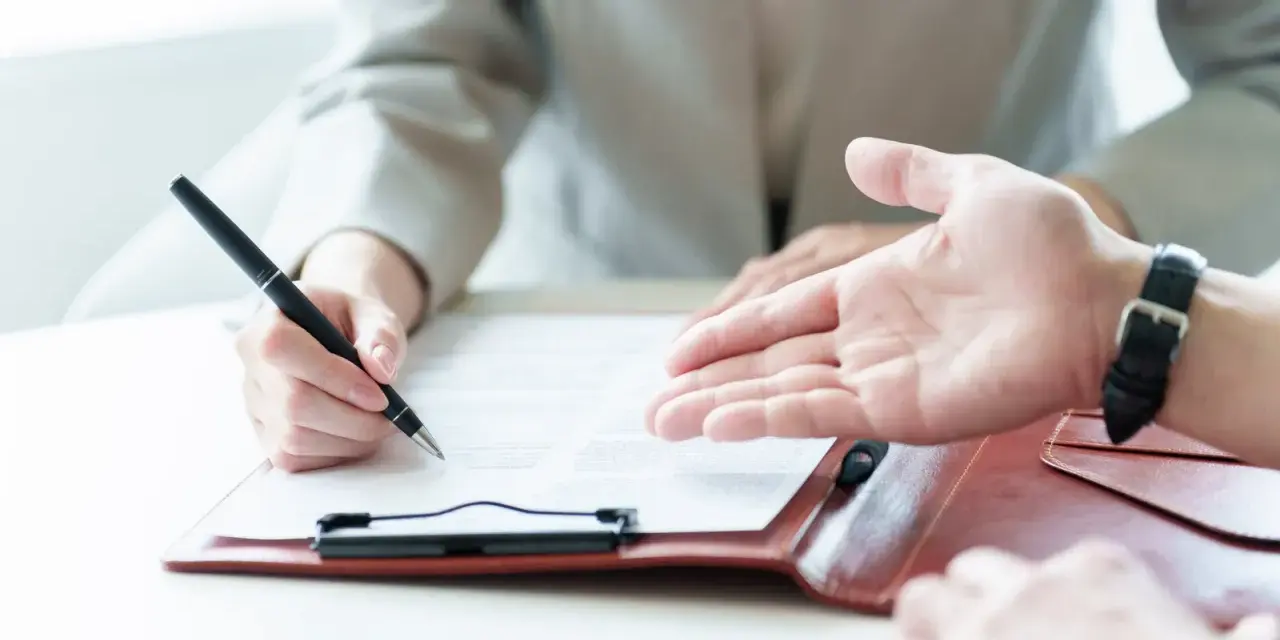 Une personne signe un contrat, discutant des conditions d'emploi avec un interlocuteur.