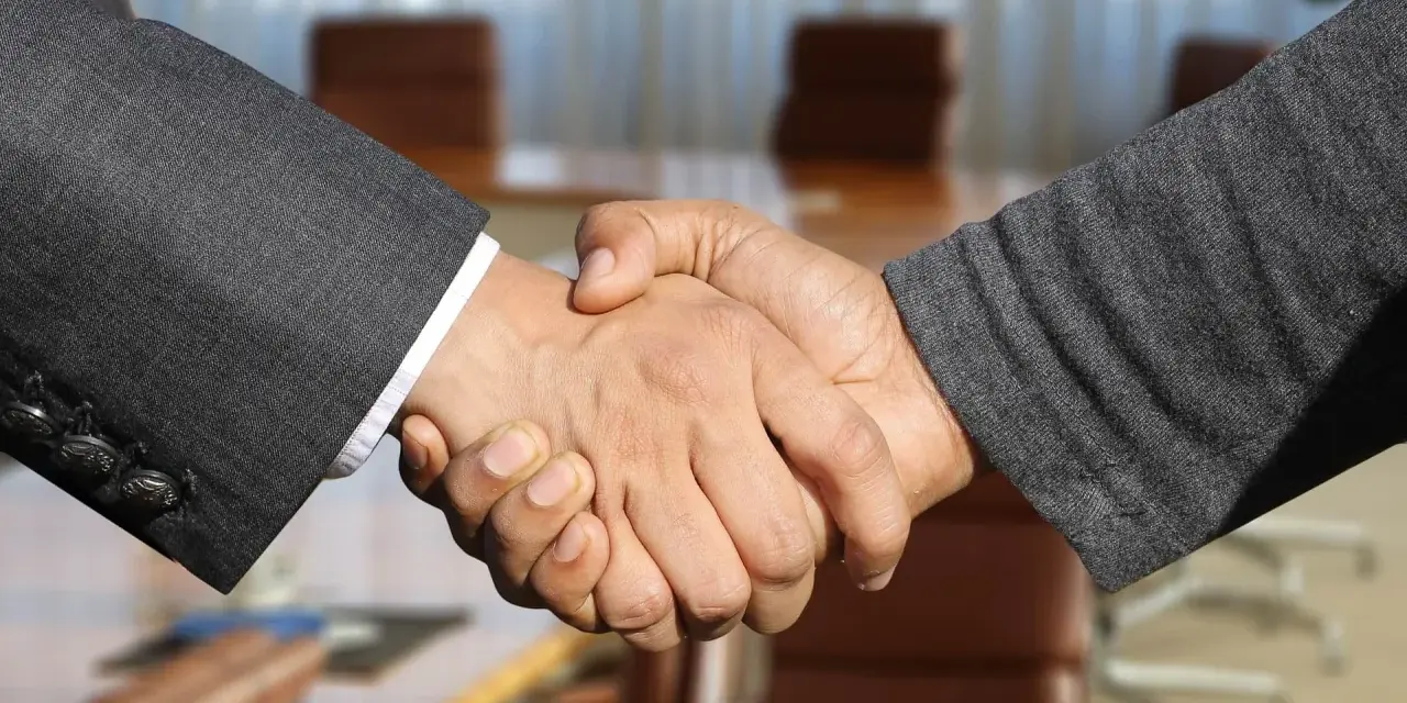 Poignée de main entre deux hommes en costume, scellant un accord. Leurs mains se serrent fermement, symbolisant la confiance et le partenariat.