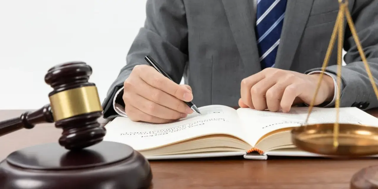 Un avocat en costume écrit dans un livre de droit, marteau de juge et balance de la justice à proximité. Une scène symbolisant l'entrave au CSE.