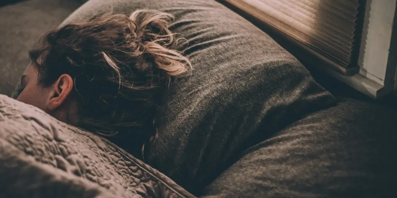 Une personne dort, peut-être suite à un licenciement pour absence injustifiée, se demandant si elle a droit au chômage.