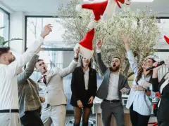 Des employés lancent des bonnets de Père Noël en l'air, célébrant joyeusement leur repas de Noël d'entreprise.