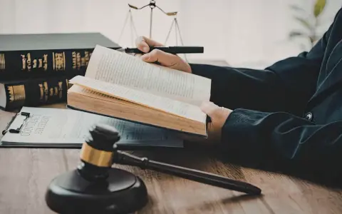 Un avocat étudie le livre de droit, cherchant la définition de l'obligation de résultat selon l'article 1231-1 du Code civil. Balance de la justice et marteau de juge en arrière-plan.