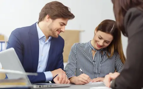 Un homme et une femme souriants discutent d'un contrat de travail étudiant. Un ordinateur portable est visible sur la table.