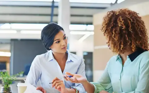 Deux femmes discutent au bureau. L'une semble expliquer les 5 obligations de l'employeur à l'autre.