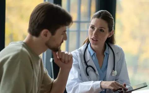 Médecin expliquant un plan de traitement à un patient lors d'une visite de pré-reprise. Le délai est respecté.