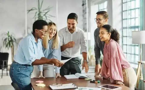 Une équipe souriante discute autour d'une table, partageant des documents. L'ambiance est détendue, comme lors d'un entretien de fin de mandat réussi.