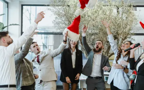 Des employés lancent des bonnets de Père Noël en l'air, célébrant joyeusement leur repas de Noël d'entreprise.