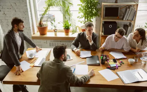 Une équipe discute autour d'une table dans un bureau lumineux, illustrant le concept de **flex office** : collaboration et adaptabilité.