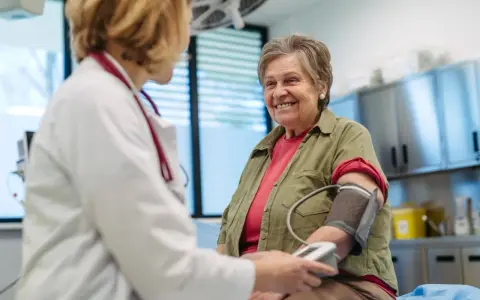 Une femme âgée souriante passe un examen de prévention santé. Le médecin lui prend la tension artérielle.