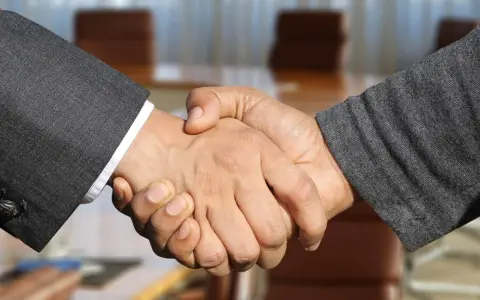 Poignée de main entre deux hommes en costume, scellant un accord. Leurs mains se serrent fermement, symbolisant la confiance et le partenariat.