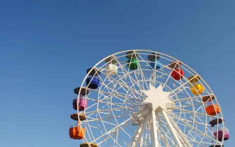 Grande roue colorée sous un ciel bleu clair, avec la lune visible. Une vue qui donne envie de monter, pour un asc cse inoubliable.