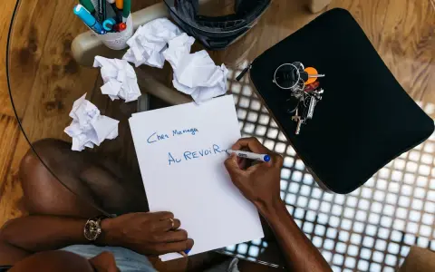 Un homme écrit "Au revoir..." sur une feuille, peut-être un mail de démission. Des brouillons froissés et des clés sont à proximité.