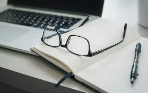 Lunettes sur un carnet ouvert, stylo et ordinateur portable. Idéal pour un congé formation professionnelle dans le privé, pour planifier son avenir.