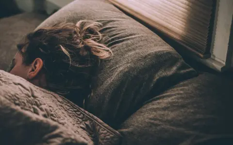 Une personne dort, peut-être suite à un licenciement pour absence injustifiée, se demandant si elle a droit au chômage.