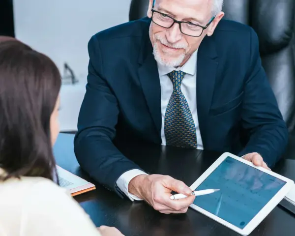 Un homme d'affaires expérimenté partage son expertise CSE en montrant un calendrier sur une tablette à une collègue.