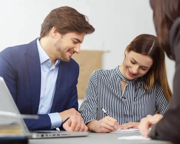 Un homme et une femme souriants discutent d'un contrat de travail étudiant. Un ordinateur portable est visible sur la table.