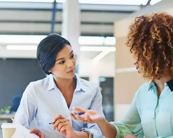 Deux femmes discutent au bureau. L'une semble expliquer les 5 obligations de l'employeur à l'autre.