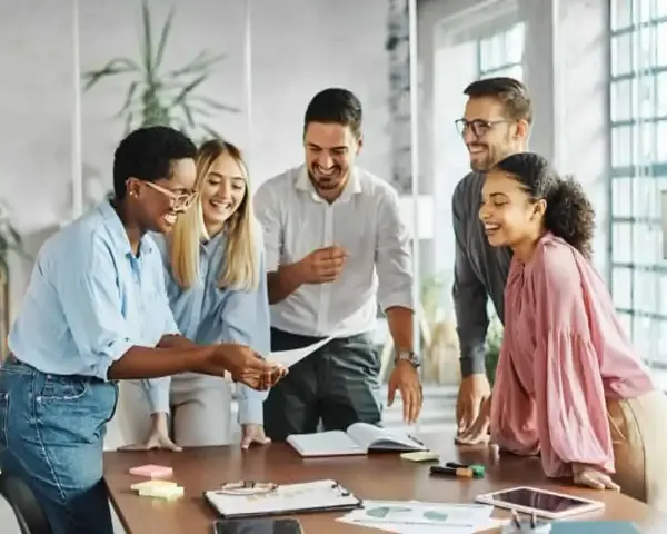 Une équipe souriante discute autour d'une table, partageant des documents. L'ambiance est détendue, comme lors d'un entretien de fin de mandat réussi.