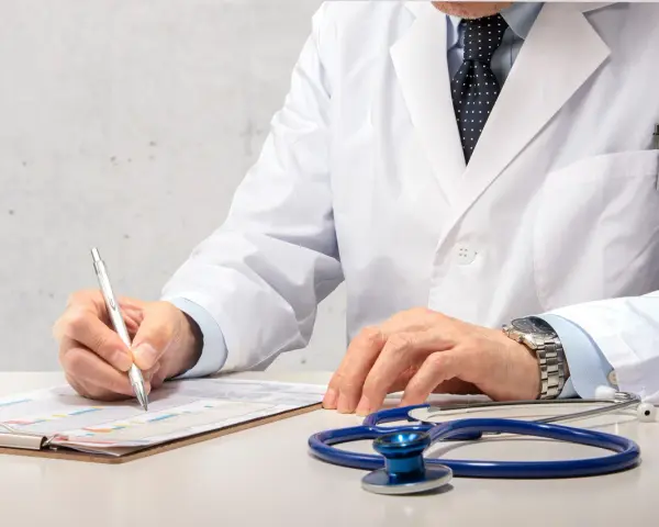 Médecin en blouse blanche rédigeant un rapport, stéthoscope à proximité. Un signalement médecine du travail est en cours.