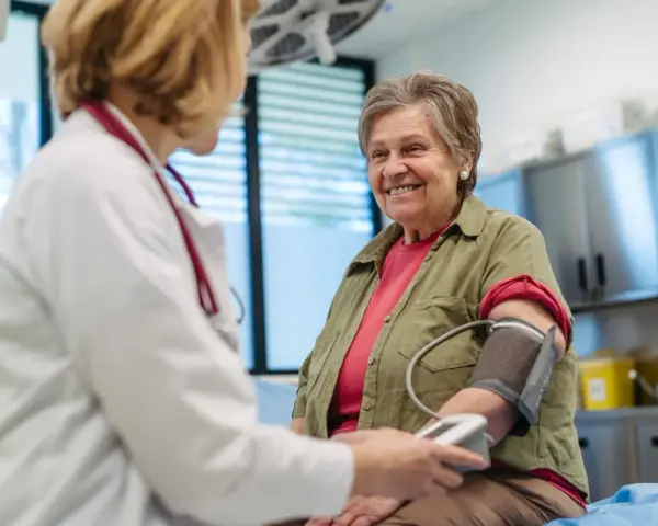 Une femme âgée souriante passe un examen de prévention santé. Le médecin lui prend la tension artérielle.