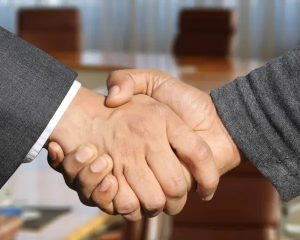 Poignée de main entre deux hommes en costume, scellant un accord. Leurs mains se serrent fermement, symbolisant la confiance et le partenariat.