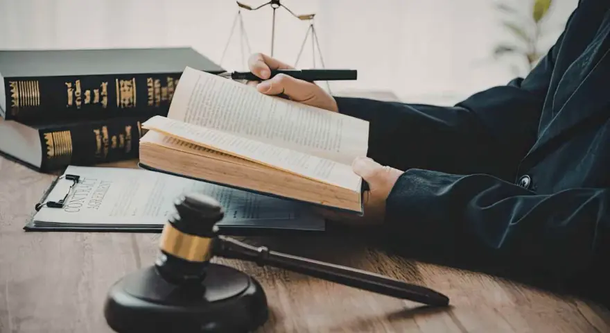 Un avocat étudie le livre de droit, cherchant la définition de l'obligation de résultat selon l'article 1231-1 du Code civil. Balance de la justice et marteau de juge en arrière-plan.