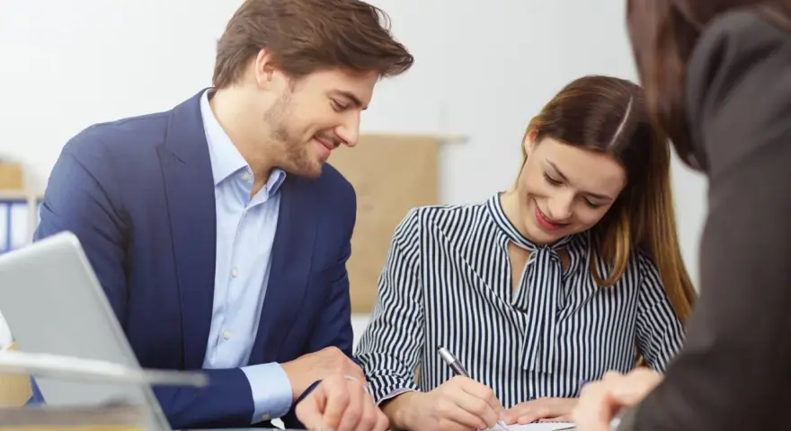 Un homme et une femme souriants discutent d'un contrat de travail étudiant. Un ordinateur portable est visible sur la table.