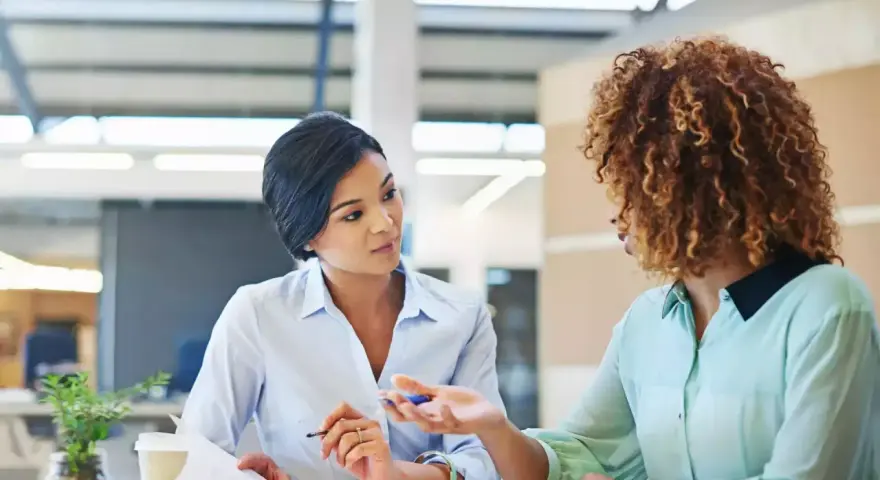 Deux femmes discutent au bureau. L'une semble expliquer les 5 obligations de l'employeur à l'autre.