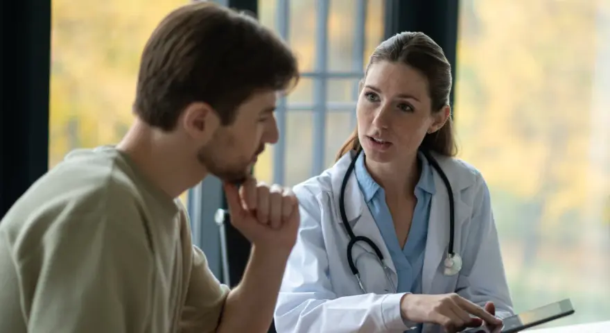 Médecin expliquant un plan de traitement à un patient lors d'une visite de pré-reprise. Le délai est respecté.