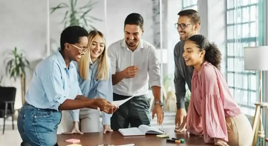 Une équipe souriante discute autour d'une table, partageant des documents. L'ambiance est détendue, comme lors d'un entretien de fin de mandat réussi.